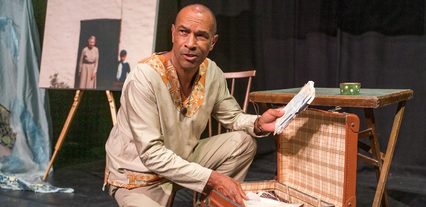 A man of dual heritage kneels next to an open suitcase of letters.